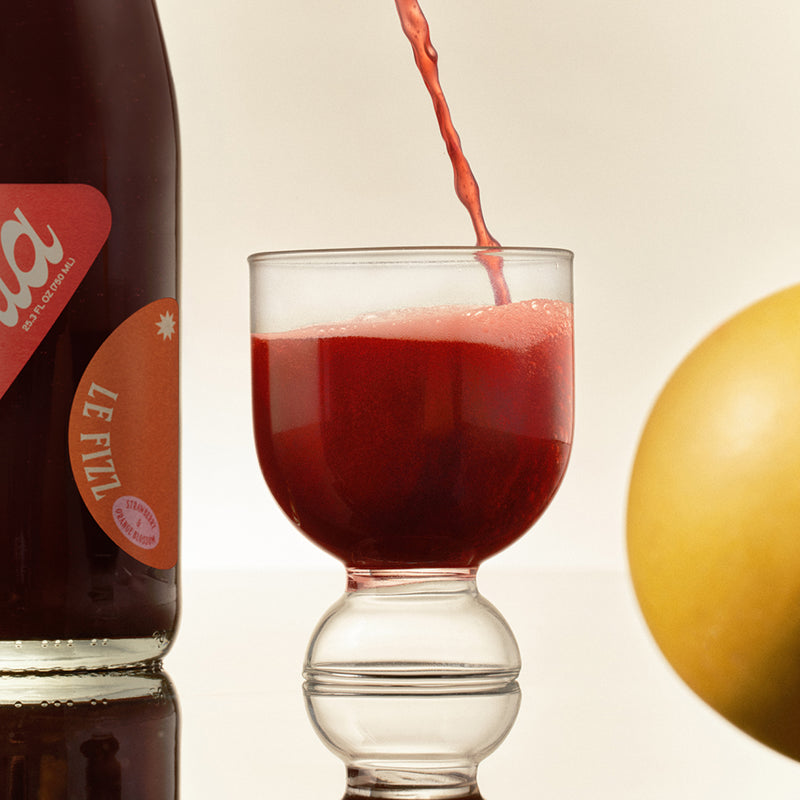 Ghia Le Fizz poured into a footed glass beside the bottle and a grapefruit