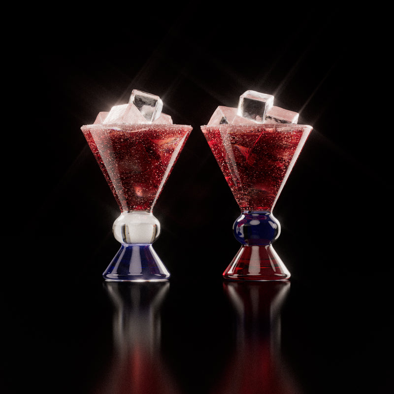 Two decorative glasses that have an amber, clear and blue base, each containing a red drink with ice cubes, highlighting the distinctive totem-inspired shape of the glasses against a light background.