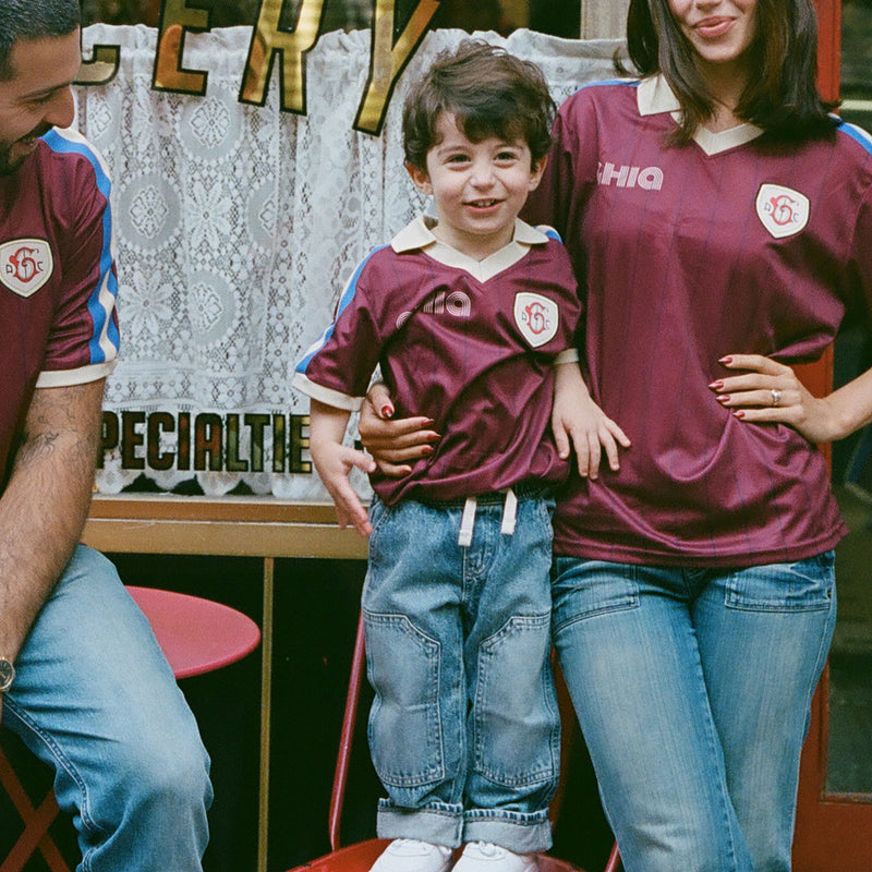 Parents and a young boy in matching maroon Ghia Jerseys posing outside a specialty grocery