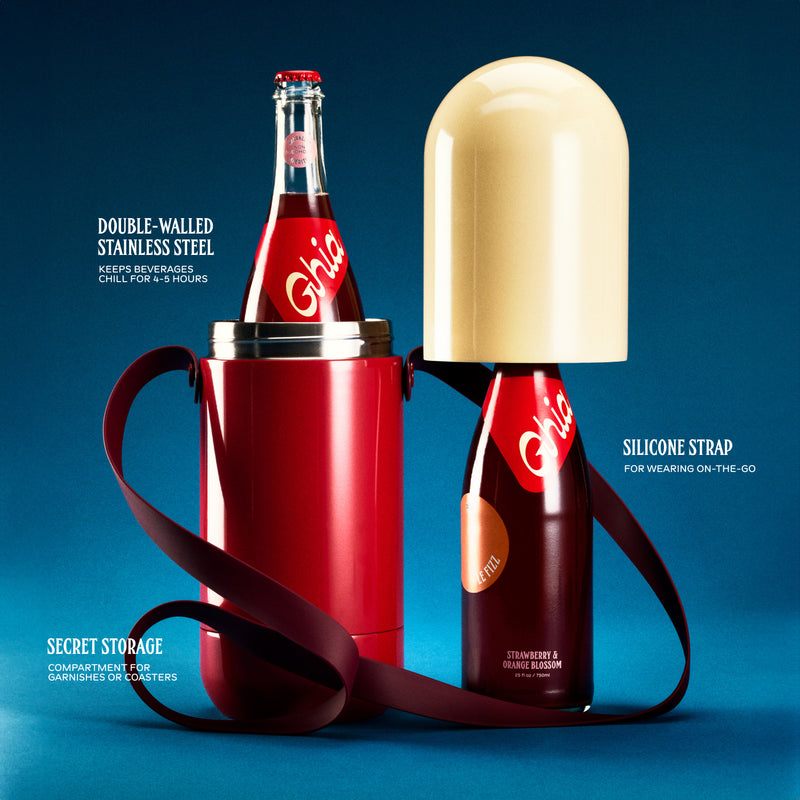 Non-alcoholic spritz in a bottle filled with a deep red strawberry and orange blossom beverage, featuring red labels alongside a red and cream colored stainless steel cooler shapped like a pill with a silicone strap.