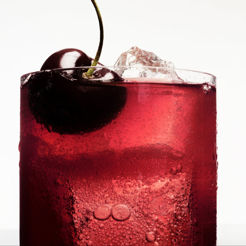 Close-up of a glass of Ghia Le Fizz over ice, deep red and bubbly, garnished with dark cherries
