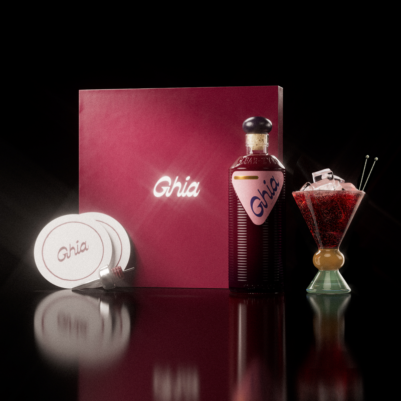 A Ghia non-alcoholic aperitif gift set with a burgundy box, paper coasters, 1 glass bottle of Berry Apéritif, and a decorative cocktail glass that has a sand and jade base.