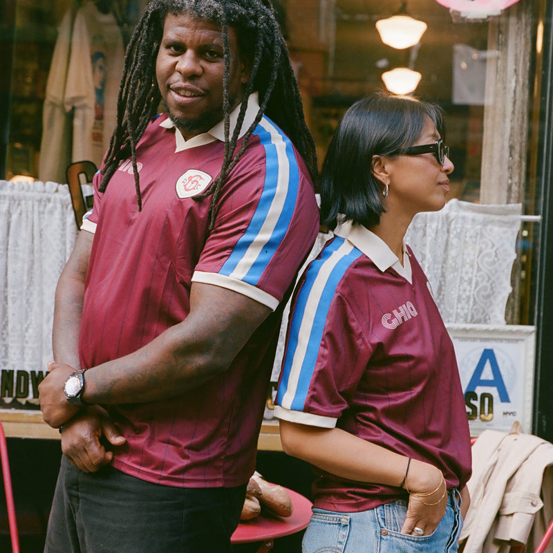 Man and woman standing back to back wearing maroon Ghia Jerseys outside a storefront