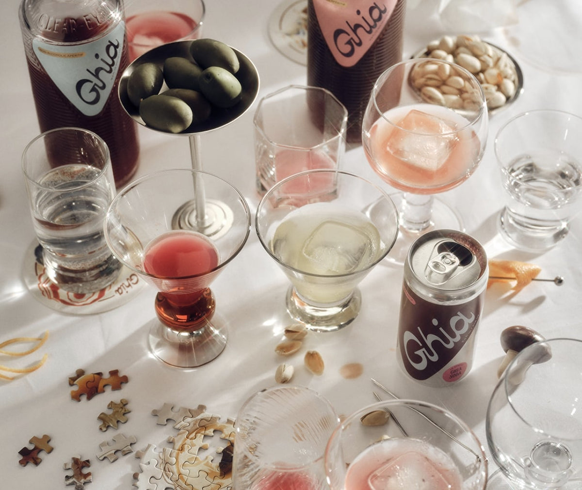 Party table with Ghia bottles, a Le Spritz can, cocktails, olives, and puzzle pieces